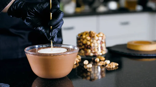 Pastry chef is dips a candy in liquid chocolate with nuts for making a cake — Stock Photo, Image