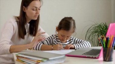 Yorgun bir anne, kızının ödevlerini yapmasına yardım ediyor.