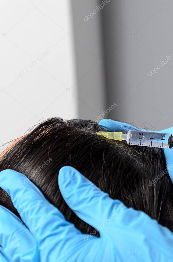 in beauty clinic cosmetician gloves making injection with a syringe in black hair roots to regenerate and give volume