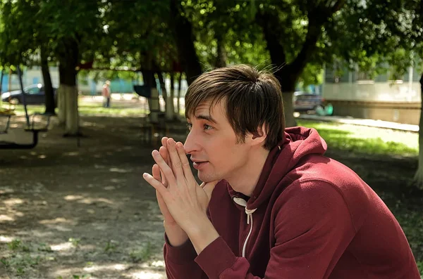 Young man on the street in the park waits and worries with a bad mood