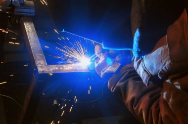 kaynakçı bir karanlık atölye kaynak metal parçalar içinde koruyucu maske içinde. Flyng kıvılcım