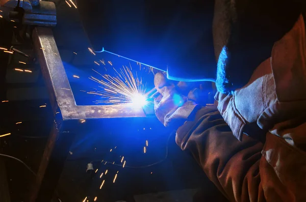 Lasser in een beschermend masker in een donkere werkvloer weld metalen onderdelen. Sparks flyng — Stockfoto