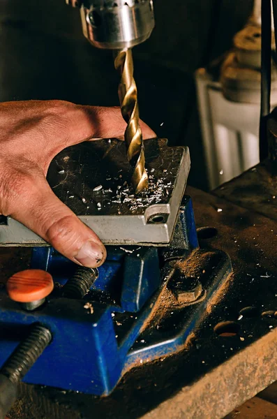 Der Arbeiter in seiner Garage arbeitet an einer Bohrmaschine. im Rahmen, eine Person in der Hand Stockbild