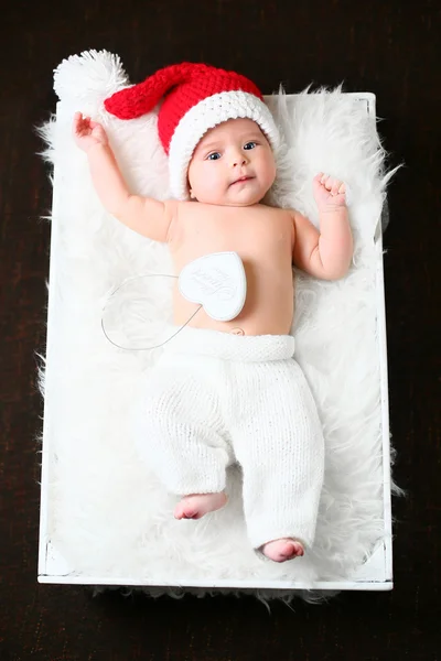 Рождественский ребенок лежит на пушистом белом одеяле в красной шляпе и белых брюках — стоковое фото