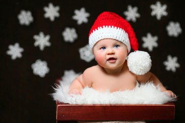 Kırmızı kuyruklu şapkalı bir beyaz tahta kutuya oturan çıktıktan bir Noel bebek