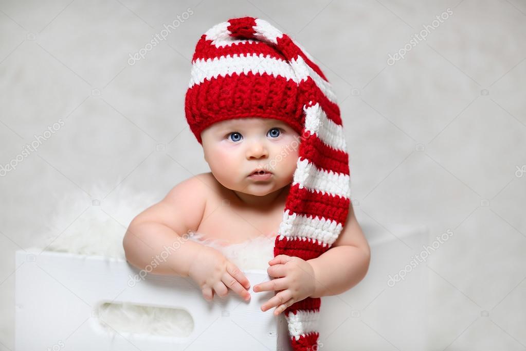 a christmas baby sitting in a white wooden box wearing a red and white striped long-tailed gnome hat