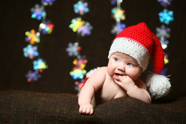 Um bebê de Natal com os dedos na boca usando um chapéu de Natal vermelho e branco — Fotografia de Stock