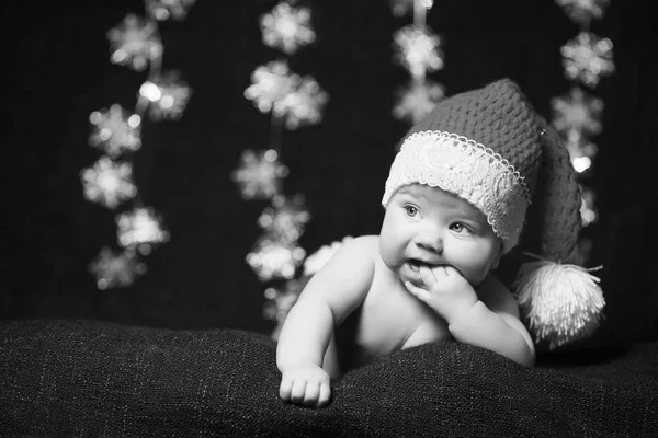 Foto em preto e branco de um bebê de Natal com os dedos na boca usando um chapéu de Natal — Fotografia de Stock