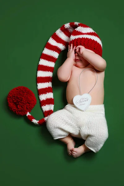 Bonito alegre natal bebê em um gnome vermelho e branco chapéu de cauda longa cobrindo o rosto com as mãos — Fotografia de Stock