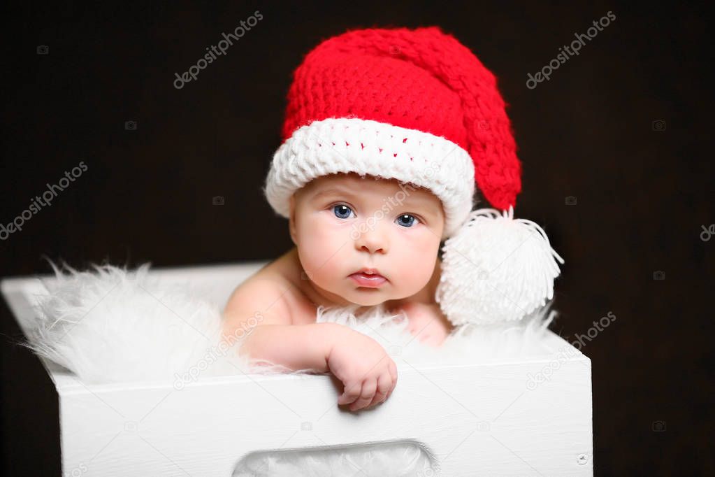 a christmas baby sitting in a white wooden box wearing a red tailed hat