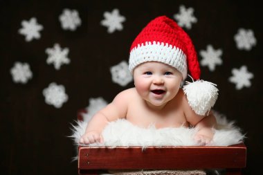 Kırmızı kuyruklu şapkalı bir kahverengi ahşap kutu içinde oturan heyecanlı bir Noel bebek