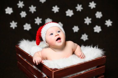 Kırmızı kuyruklu şapkalı bir kahverengi ahşap kutu içinde oturan heyecanlı bir Noel bebek