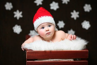 Kırmızı kuyruklu şapkalı bir kahverengi ahşap kutu içinde oturan endişeli Noel bebek