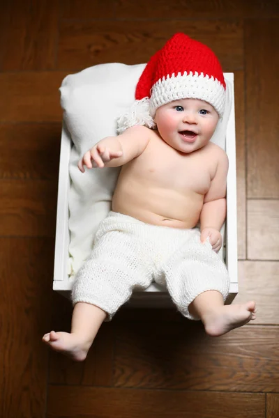 Um bebê de Natal deitado em uma caixa branca fofa usando um chapéu de cauda vermelha e calças brancas — Fotografia de Stock