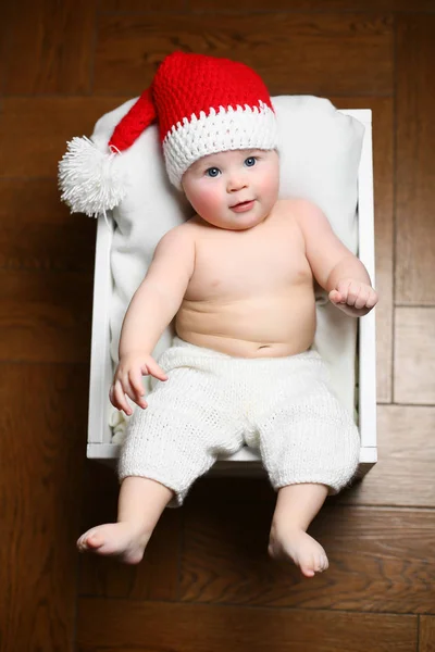 Рождественский ребенок лежит на пушистой белой коробке в красной шляпе и белых брюках — стоковое фото