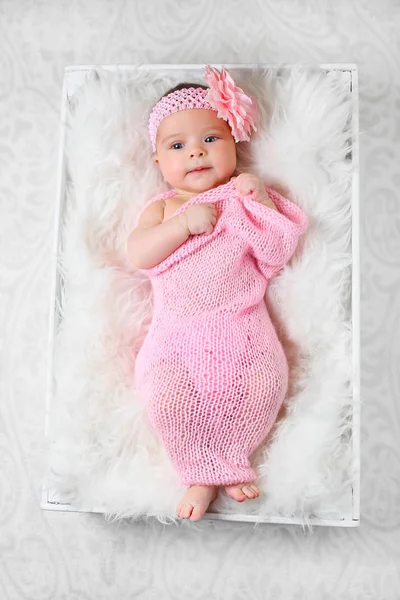 Bonito pequena menina com uma flor rosa headband deitado em um cobertor macio branco envolto em uma toalha de queijo rosa — Fotografia de Stock