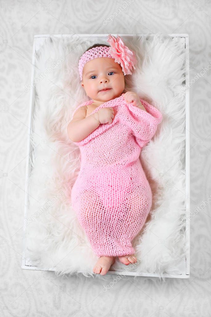 cute little baby girl with a pink flower headband lying on a white fluffy blanket wrapped in a pink cheesecloth