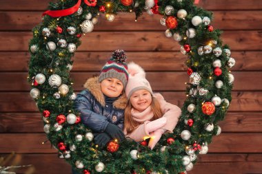 mutlu küçük erkek ve kız bir şekilde dekore edilmiş Noel çelenk ahşap arka plan üzerinde poz 