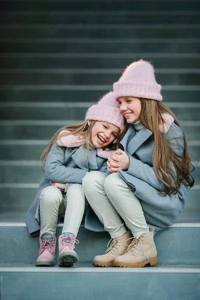 two adorable little sisters hugging sitting on concrete stairs outdoors