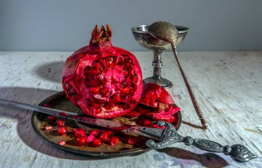 Gümüş bir tabakta büyük, olgun, kırmızı bir leğen ve güzel bir hançer. İştah açıcı kırmızı taneler tabaklara saçılmış..