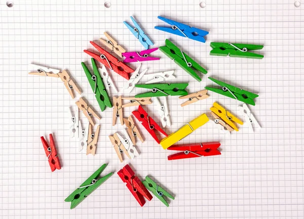 Wooden clothespins of different colors and different sizes lie on a sheet of notepad. Bright colors.