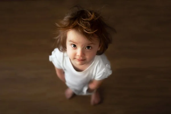 Ein kleines zotteliges Mädchen mit großen Augen steht auf und schaut auf. Ansicht von oben aus nächster Nähe. — Stockfoto