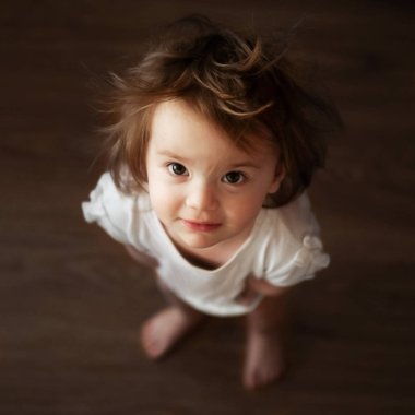 Büyük gözlü küçük tüylü kız ayağa kalkıyor ve yukarı bakıyor. Üst görünüm kapat