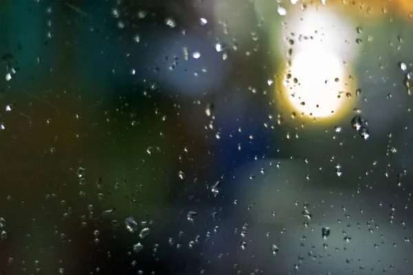 Des lumières de ville floues avec de la pluie tombent au premier plan. Lumières colorées non concentrées derrière le verre avec des gouttes. Lumières brillantes de bokeh de nuit .. — Photo