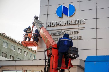 Norilsk, Russia - March 5, 2020: the operator controls the crane, workers hang a sign on the building