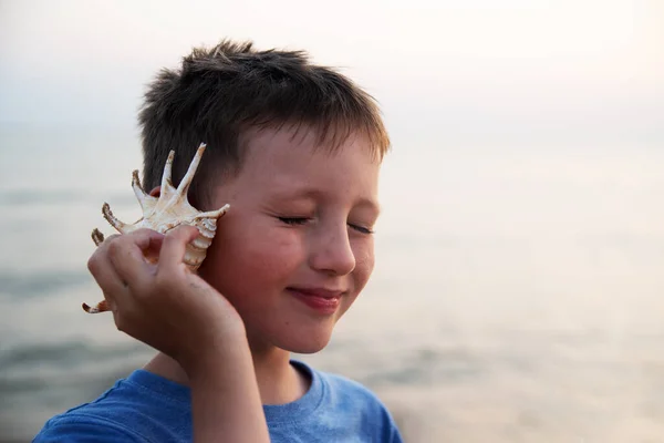 Kör bir çocuk, kulağına deniz kabuğu dayamış denizin sesini dinler.