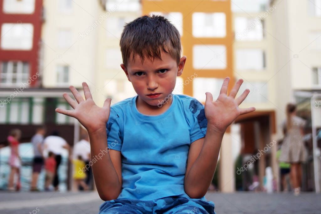 A little boy sits on the ground with his hands up and protests. The concept of raising a difficult naughty child.