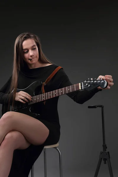 Hermosa chica afinando cuerdas en la guitarra eléctrica — Foto de Stock