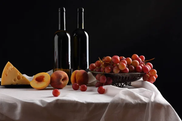 Bottles of wine, cheese and fruit on a dark background