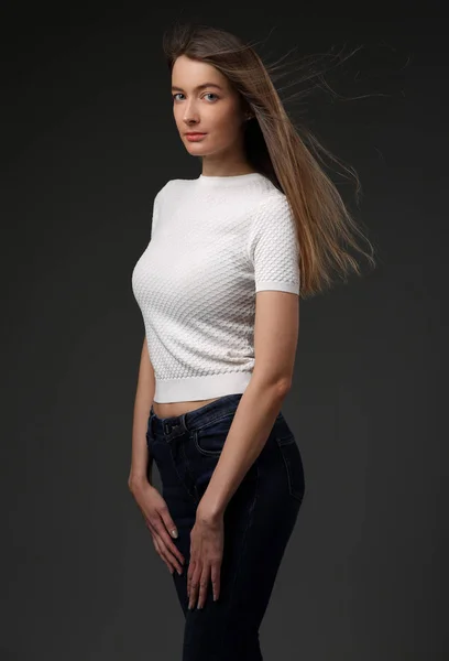 Menina bonita em uma camiseta branca e jeans em um fundo cinza — Fotografia de Stock