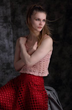 Gri bir arka planda pembe bluz ve kırmızı etekli güzel bir kızın stüdyo portresi.