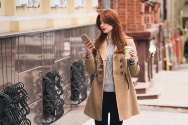 Görüşmek üzere! Açık havada yürürken gülümseme ile cep telefonu ekranına bakarak güzel genç kadın.