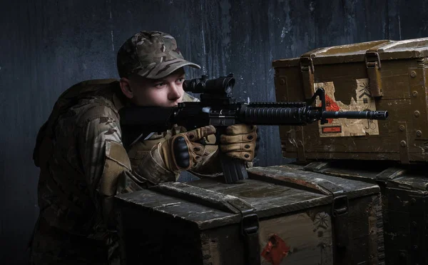 A treinar nos cortinados. Homem de uniforme militar com espingarda de assalto apontando para o alvo no fundo da parede escura. Coaching in-dash . — Fotografia de Stock