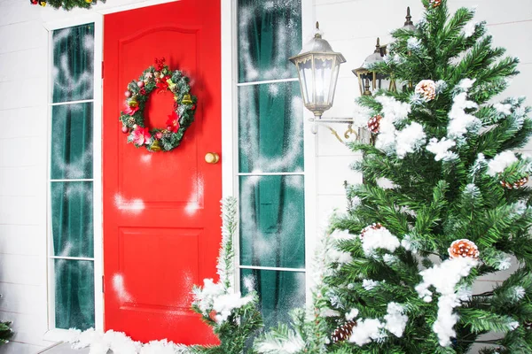 Corona de Navidad con adornos, conos y ramas de hoja perenne en una puerta roja . — Foto de Stock