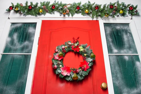 Corona de Navidad con adornos, conos y ramas de hoja perenne en una puerta roja . — Foto de Stock