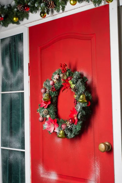 Couronne de Noël avec des boules, des cônes et des branches persistantes sur une porte rouge . — Photo
