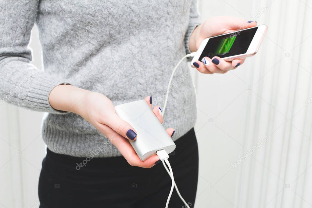 Girl's hand holding large silver aluminum power bank (external battery) as a symbol of mobile energy and electric equipment in modern design.