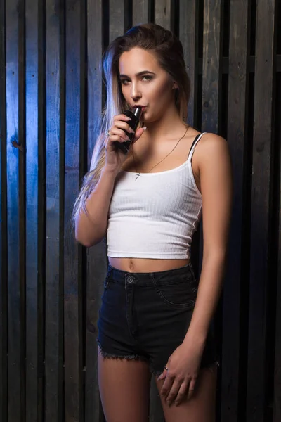 Jovem mulher loira bonita fumando, vaping e-cigarro com fumaça no fundo de madeira . — Fotografia de Stock