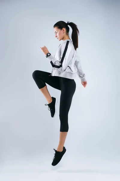 Retrato de cuerpo entero de una joven fitness en ropa deportiva posando y saltando aislada sobre fondo gris —  Fotos de Stock