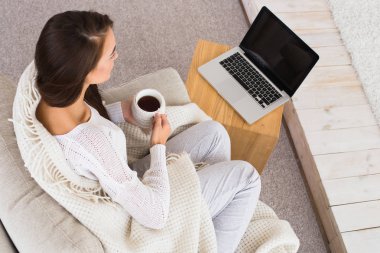 Sabah kahve veya çay fincan keyfini çıkarın. Dizüstü ekran üzerinde seyir ve sabah haberleri izlerken güzel kadın.