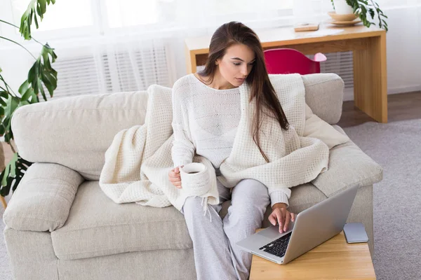 Surfer sur le net à la maison. Belle jeune femme utilisant un ordinateur portable tout en étant assis à l'entraîneur à la maison — Photo