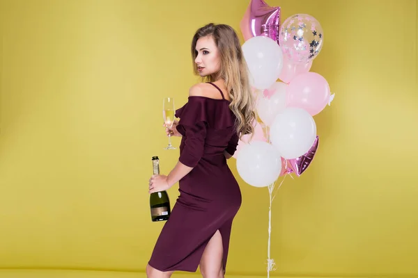 Mulher bonita e atraente em vestido marsala com garrafa e copo de champanhe. Jovem feliz comemorar aniversário em balões de fundo — Fotografia de Stock