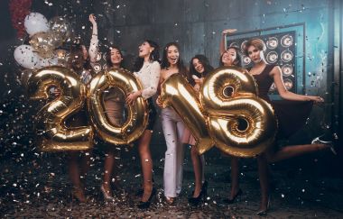 Yeni yıl partisi kutluyor. Güzel taşıyan altın renkli numaraları 2018 giyen ve konfeti atma neşeli genç kız grup