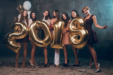 Yeni yıl partisi kutluyor. Güzel neşeli genç kız grup taşıyan altın renkli numaraları 2018 giyiyor 
