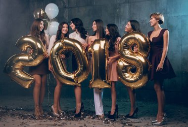 Yeni yıl partisi kutluyor. Güzel neşeli genç kız grup taşıyan altın renkli numaraları 2018 giyiyor 