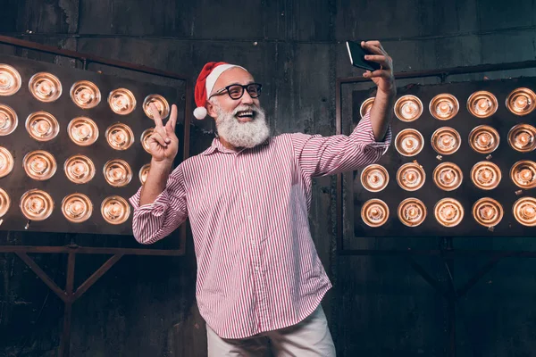 Glücklich moderner Weihnachtsmann macht Selfie auf der Silvesterparty und zeigt zwei Finger. bärtiger Modemann hat Spaß an Weihnachten, während er auf Freunde wartet. — Stockfoto